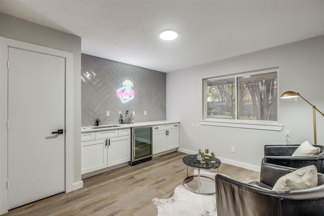 bar with sink, wine cooler, light hardwood / wood-style floors, decorative backsplash, and white cabinets