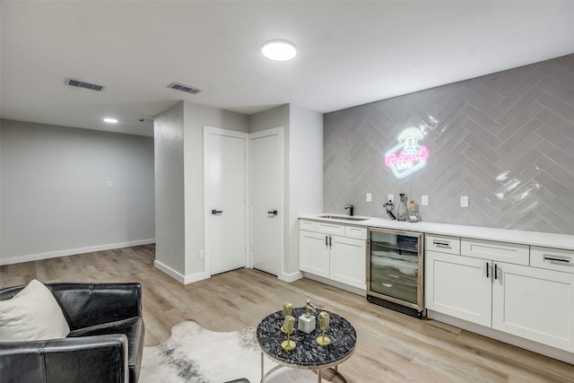 bar featuring wine cooler, light hardwood / wood-style flooring, white cabinets, and sink