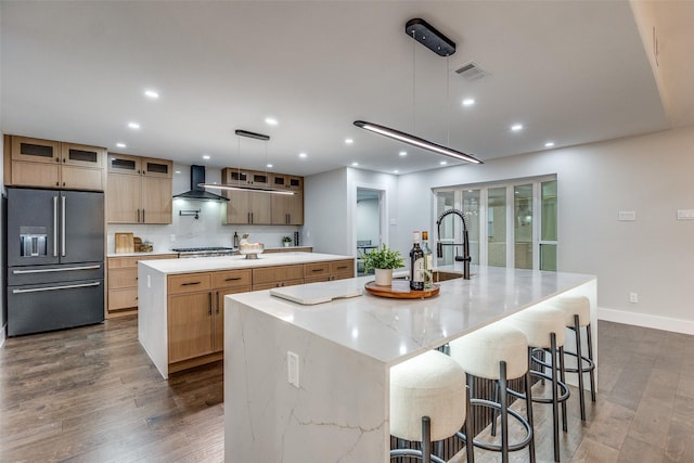 kitchen with hanging light fixtures, stainless steel appliances, wall chimney range hood, a kitchen breakfast bar, and a spacious island