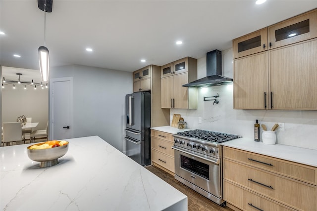 kitchen featuring high end appliances, wall chimney range hood, light stone counters, and light brown cabinetry