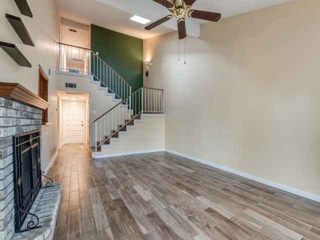 unfurnished living room featuring hardwood / wood-style flooring, ceiling fan, a high ceiling, and a brick fireplace