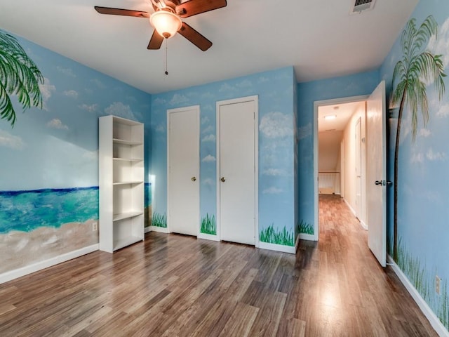 unfurnished bedroom featuring ceiling fan, wood-type flooring, and multiple closets