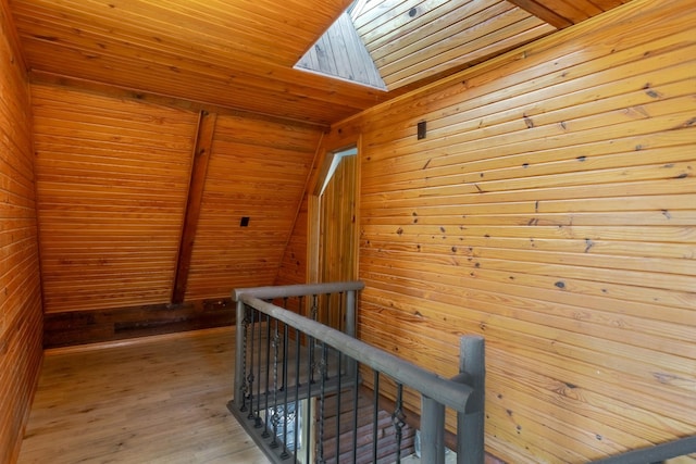 corridor with light wood-type flooring, a skylight, wooden ceiling, and wooden walls