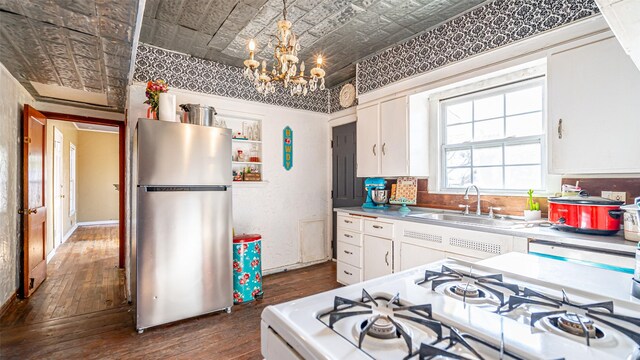 kitchen with stainless steel fridge, sink, decorative light fixtures, range, and white cabinetry