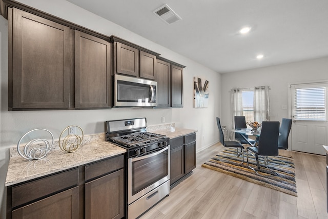 kitchen featuring dark brown cabinets, light hardwood / wood-style floors, light stone countertops, and appliances with stainless steel finishes