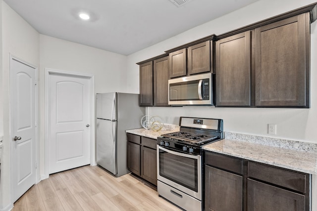 kitchen with light stone countertops, appliances with stainless steel finishes, dark brown cabinetry, and light hardwood / wood-style floors