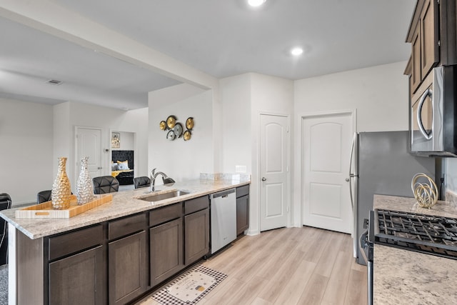 kitchen with dark brown cabinetry, sink, stainless steel appliances, light stone counters, and light hardwood / wood-style flooring