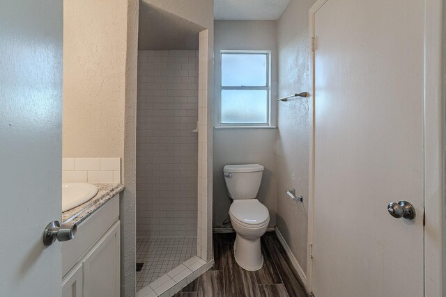 bathroom featuring toilet, a tile shower, hardwood / wood-style floors, and vanity