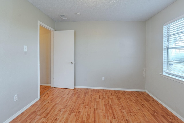 spare room with light wood-type flooring and a textured ceiling