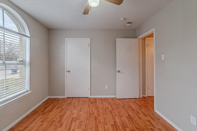 unfurnished bedroom with ceiling fan, a textured ceiling, a closet, and light wood-type flooring