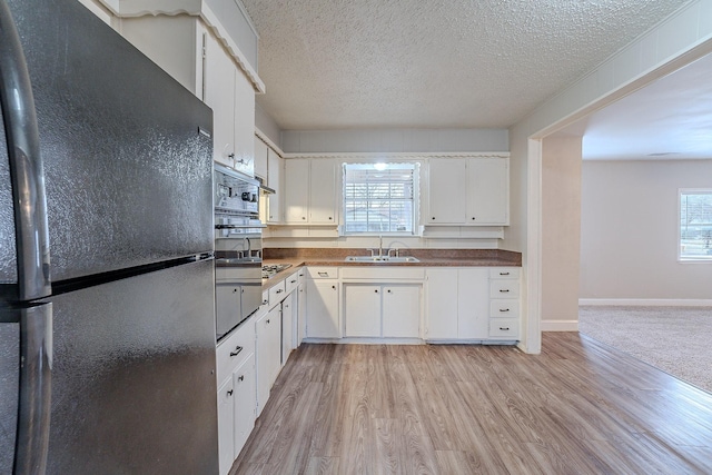 kitchen with black fridge, white cabinetry, light hardwood / wood-style floors, and sink