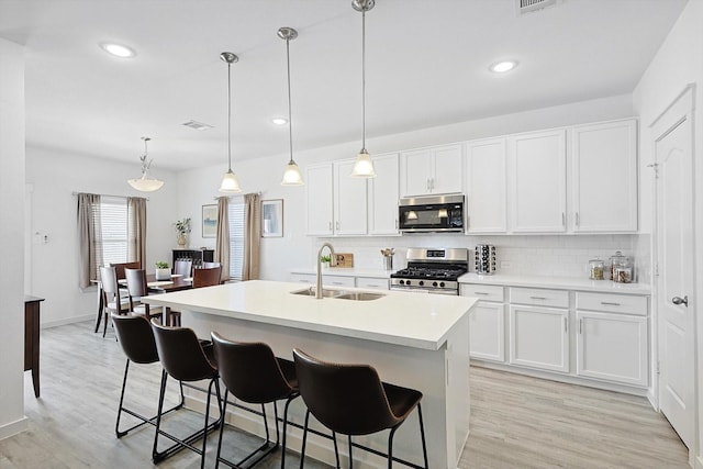 kitchen with white cabinets, decorative light fixtures, an island with sink, and appliances with stainless steel finishes