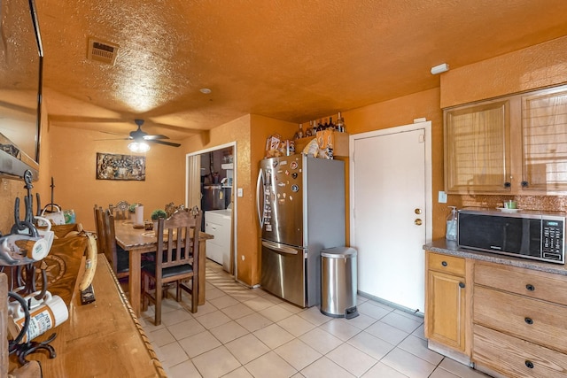 kitchen with ceiling fan, light tile patterned floors, a textured ceiling, stainless steel refrigerator, and washer / clothes dryer