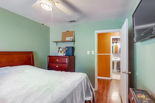 bedroom featuring light wood-type flooring, ensuite bathroom, ceiling fan, and sink