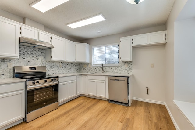 kitchen featuring appliances with stainless steel finishes, light hardwood / wood-style floors, sink, white cabinetry, and backsplash