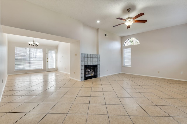 unfurnished living room featuring ceiling fan with notable chandelier, a tile fireplace, a textured ceiling, and light tile patterned floors