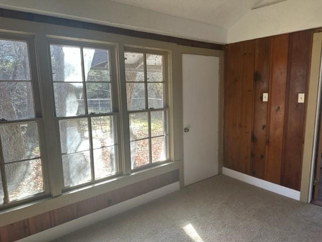 interior space featuring carpet, vaulted ceiling, and wooden walls