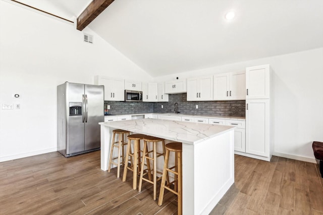 kitchen featuring light stone countertops, appliances with stainless steel finishes, beam ceiling, white cabinets, and a center island