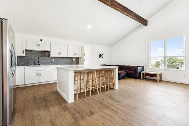 kitchen with white cabinetry, a center island, a kitchen breakfast bar, vaulted ceiling with beams, and stainless steel fridge