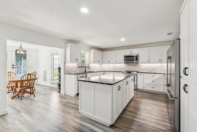 kitchen with white cabinets, hardwood / wood-style floors, stainless steel appliances, and a kitchen island