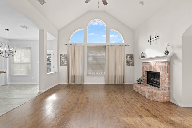 unfurnished living room with hardwood / wood-style floors, ceiling fan with notable chandelier, a brick fireplace, and a wealth of natural light