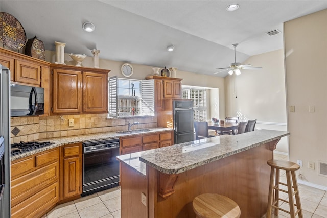 kitchen featuring sink, a center island, light tile patterned floors, a kitchen breakfast bar, and black appliances