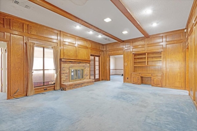 unfurnished living room with a fireplace, wooden walls, beamed ceiling, light colored carpet, and built in shelves