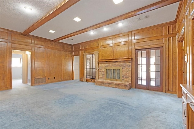 unfurnished living room with beam ceiling, french doors, light colored carpet, and a brick fireplace