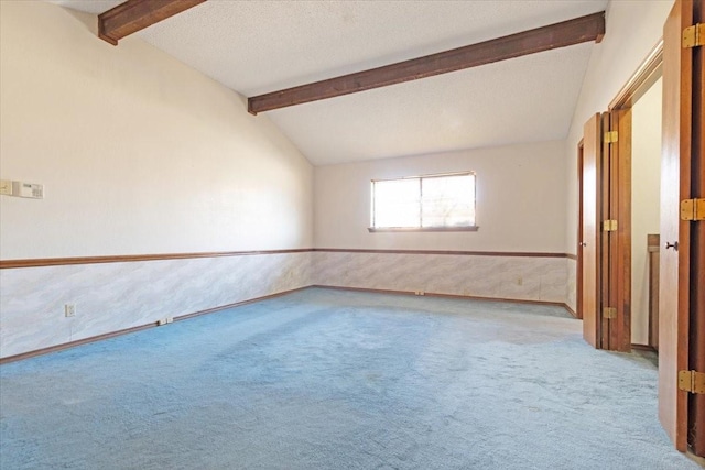 carpeted empty room with lofted ceiling with beams and a textured ceiling