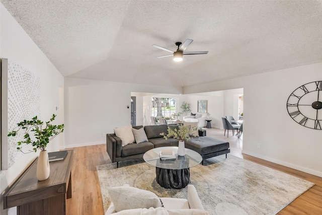 living room with ceiling fan, light hardwood / wood-style floors, a textured ceiling, and vaulted ceiling