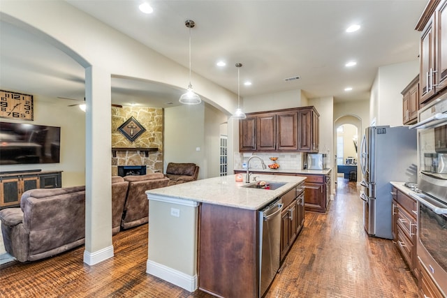 kitchen featuring a kitchen island with sink, stainless steel appliances, pendant lighting, a fireplace, and sink