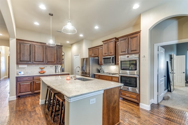 kitchen with sink, light stone counters, backsplash, a center island with sink, and appliances with stainless steel finishes