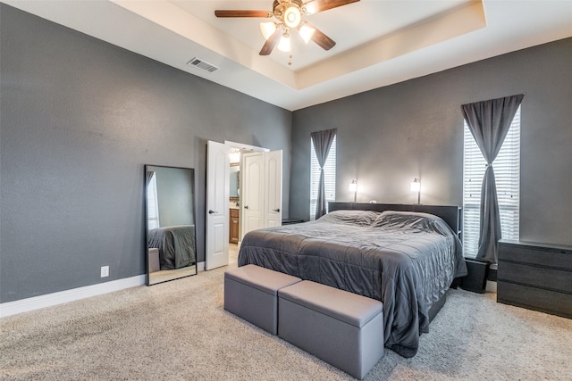 bedroom with multiple windows, light carpet, ceiling fan, and a tray ceiling