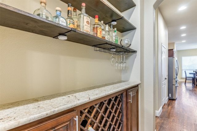 bar with dark hardwood / wood-style floors, light stone counters, and stainless steel fridge