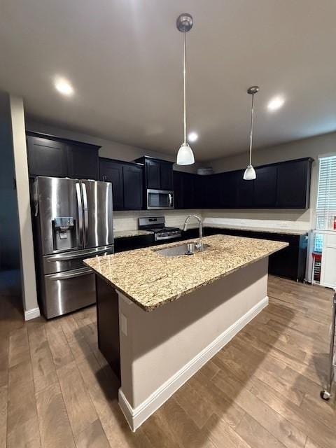 kitchen featuring pendant lighting, appliances with stainless steel finishes, light hardwood / wood-style flooring, sink, and a center island with sink