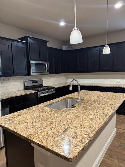 kitchen with hanging light fixtures, stainless steel appliances, and an island with sink