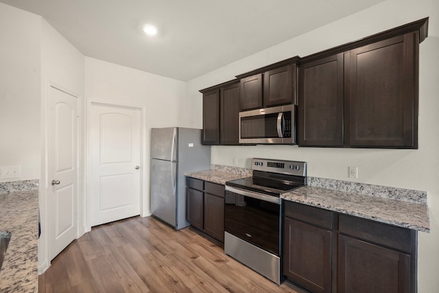 kitchen featuring dark brown cabinets, light wood-type flooring, light stone countertops, and stainless steel appliances