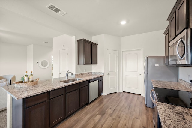 kitchen featuring dark brown cabinetry, light stone countertops, sink, appliances with stainless steel finishes, and light wood-type flooring