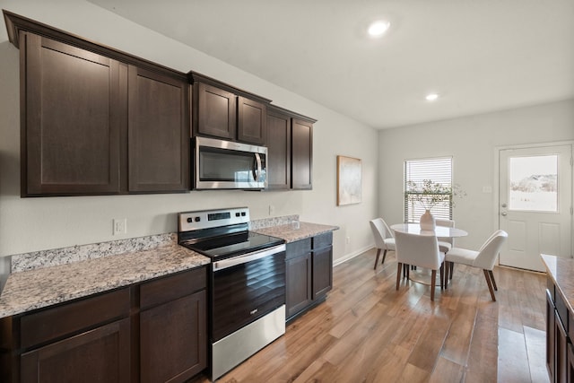 kitchen with light stone countertops, dark brown cabinets, stainless steel appliances, and light hardwood / wood-style floors