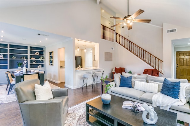 living room featuring vaulted ceiling, hardwood / wood-style flooring, built in shelves, ceiling fan, and ornamental molding