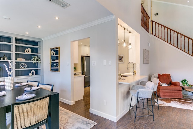 dining area with crown molding, built in features, sink, and dark wood-type flooring