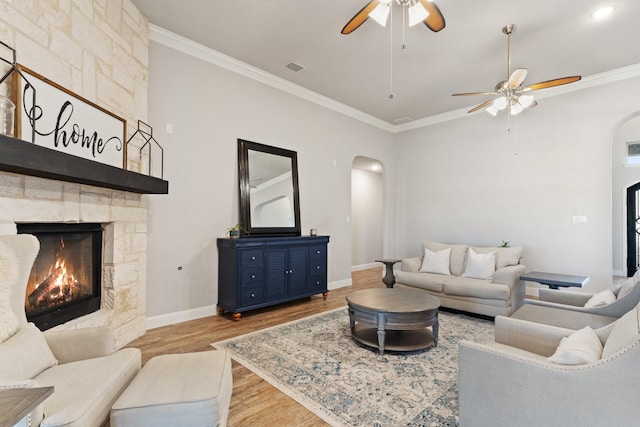 living room featuring light wood-type flooring, a stone fireplace, ceiling fan, and ornamental molding