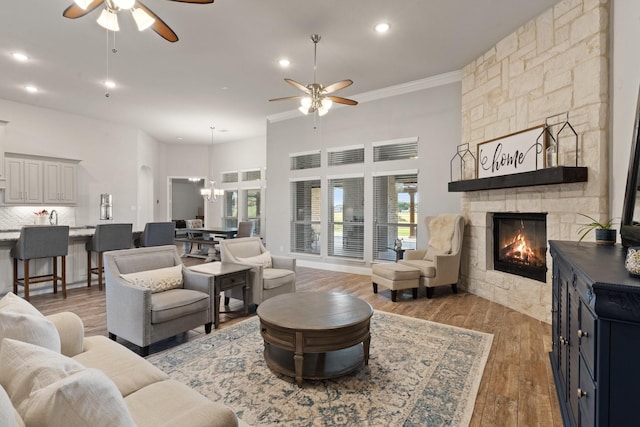 living room with a fireplace, light wood-type flooring, ceiling fan with notable chandelier, and crown molding