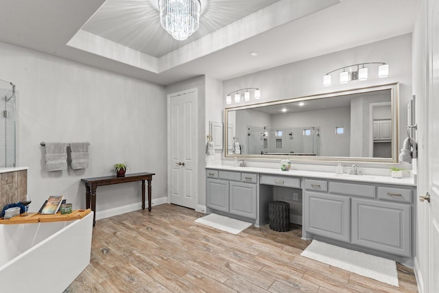 bathroom with an inviting chandelier, separate shower and tub, a tray ceiling, vanity, and hardwood / wood-style flooring