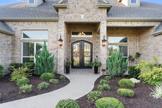 view of exterior entry featuring brick siding, roof with shingles, and french doors