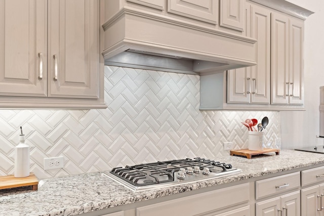 kitchen with decorative backsplash, light stone countertops, stainless steel gas stovetop, and custom exhaust hood