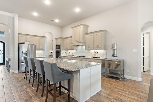 kitchen with appliances with stainless steel finishes, a kitchen breakfast bar, tasteful backsplash, light stone counters, and a center island with sink