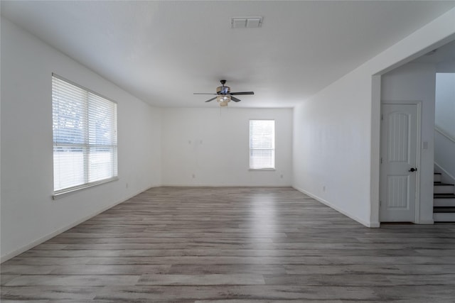 unfurnished room featuring ceiling fan, wood finished floors, visible vents, baseboards, and stairs