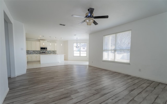 unfurnished living room with light wood-type flooring, recessed lighting, baseboards, and ceiling fan with notable chandelier