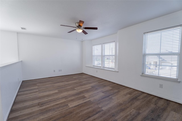 spare room featuring a ceiling fan, visible vents, dark wood finished floors, and baseboards